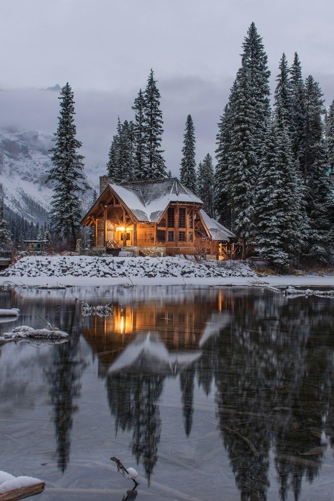 wooden house near pine trees and pond coated with snow during daytime