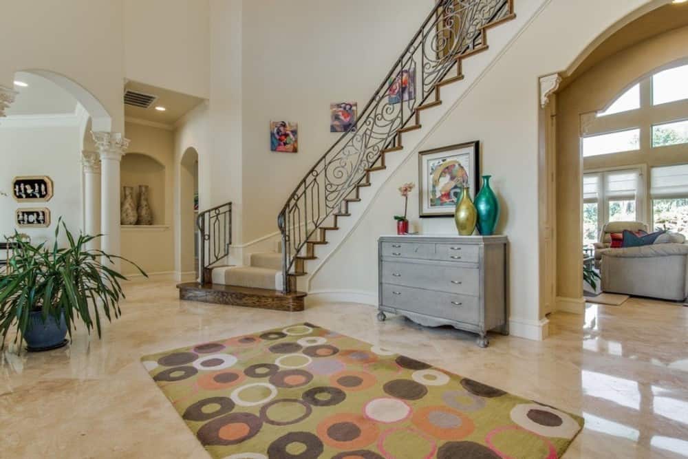 The foyer includes an ornate winding staircase and a console table topped with metallic vases and a framed artwork.