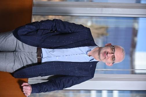 A person in a suit standing in front of a window

Description automatically generated