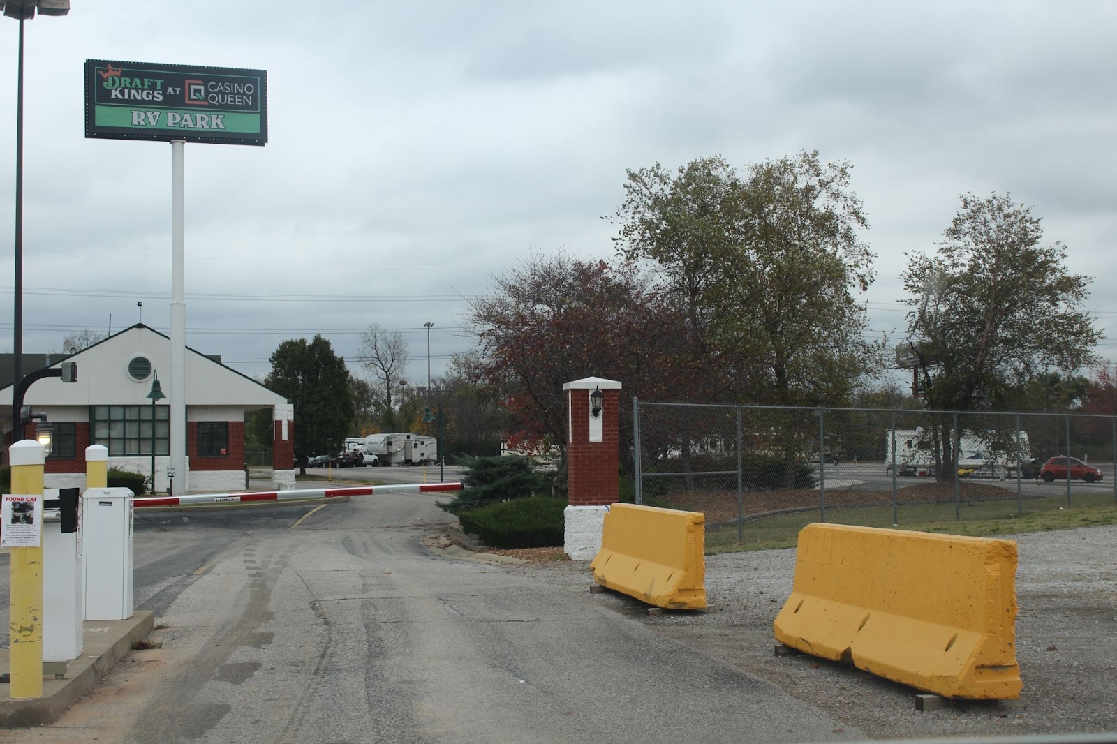 Image: The photo shows the entrance to an RV park. There are yellow road blockers in the foreground, and a road leads past them towards RVs in the background. Treasure Shields Redmond, Casino Queen RV Park, East St. Louis, 2024. 