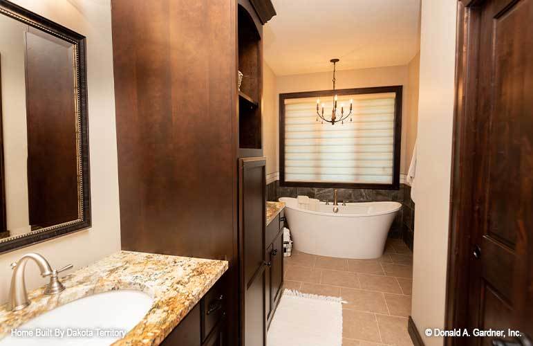 The primary bathroom is equipped with his and her vanities along with a freestanding tub illuminated by a candle chandelier.