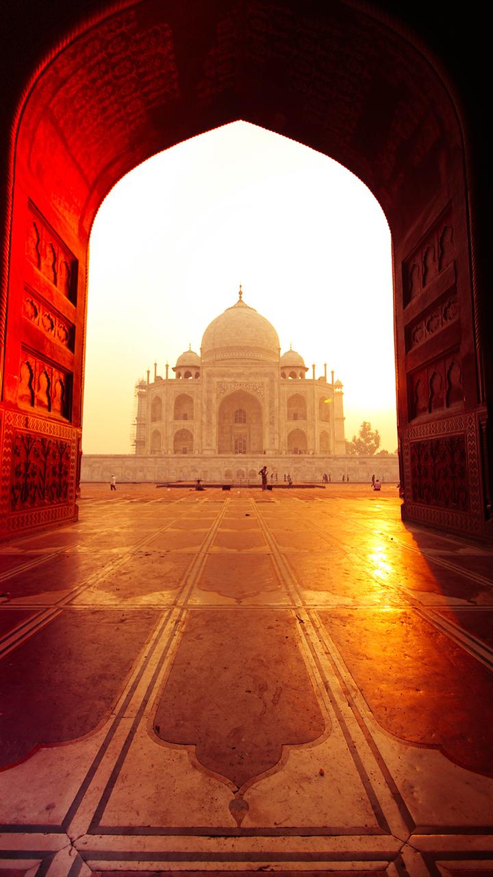 At sunrise, the Taj Mahal, an architectural masterpiece in Agra, is framed by an ornately carved archway.