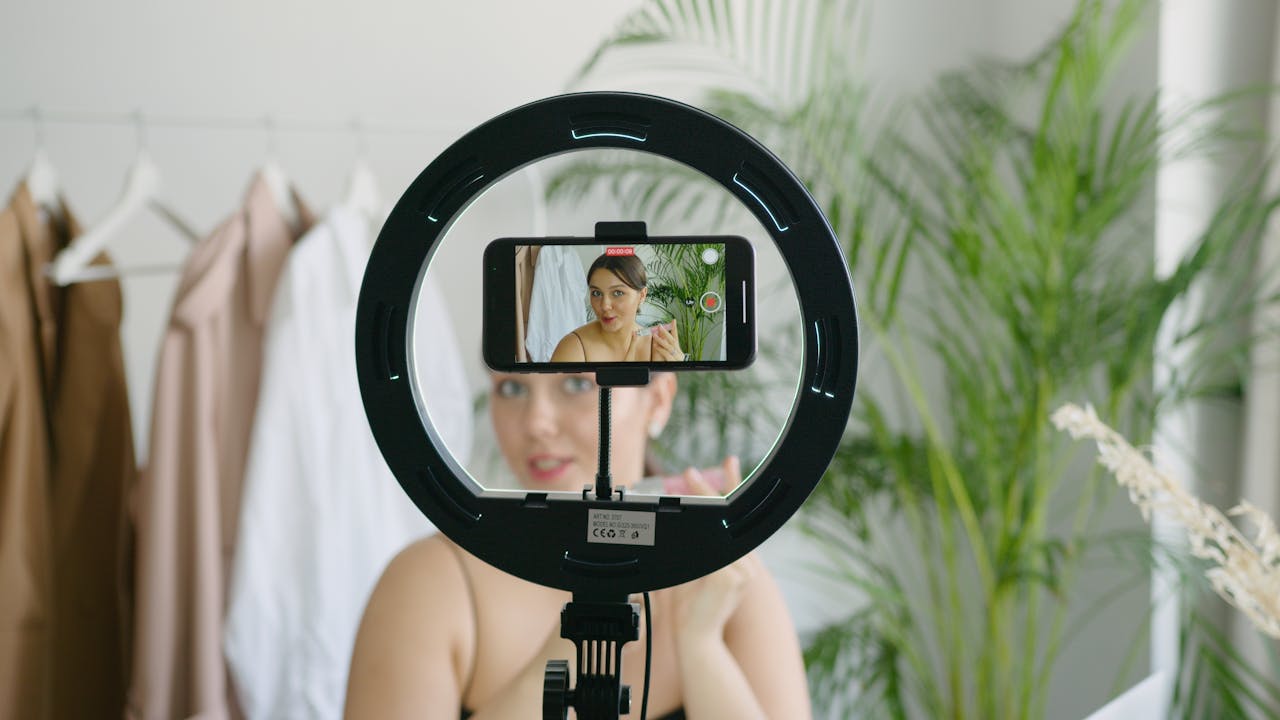 A woman snaps a selfie with a camera positioned on a ring light, showcasing her radiant smile and well-lit features.