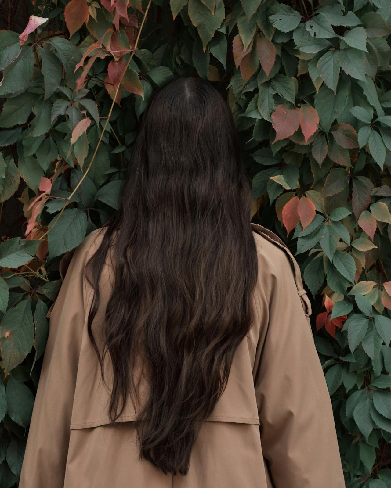 Woman with long, natural-looking dark brown hair standing against leafy background