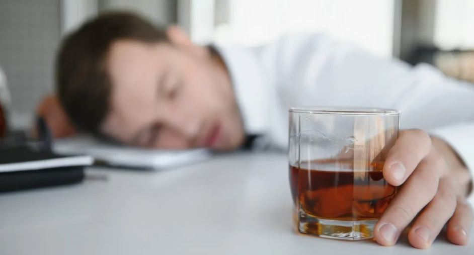 A person sleeping on a table with a glass of liquid

Description automatically generated