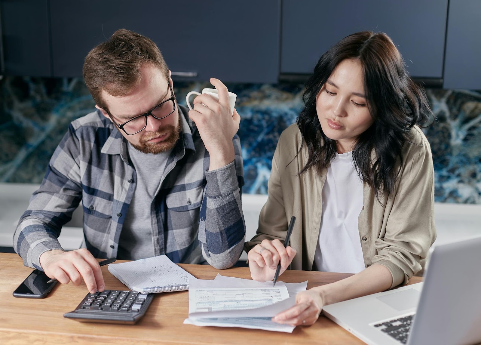 Un hombre y una mujer están trabajando juntos en una mesa, analizando facturas y utilizando una calculadora