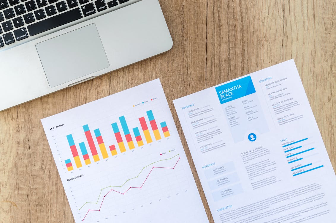 Free Top view of a laptop, charts, and resume on a wooden desk, showcasing business analysis and job application. Stock Photo