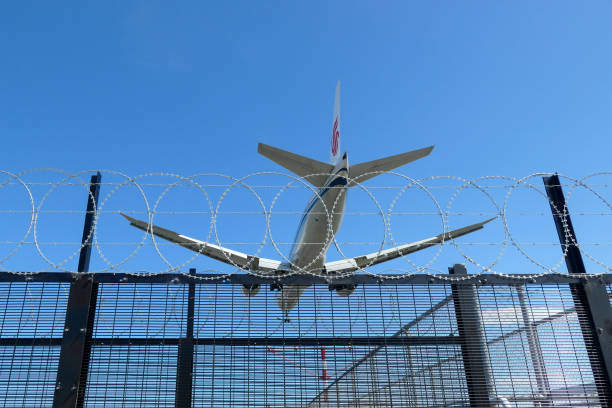 Air China Razor Wire Circles An Air China Boeing B777-39L(ER) plane, registration B-1266, coming into land over razor wire and steel fencing surrounding a navigational landing light structure at Sydney Kingsford-Smith Airport as flight CA173 from Beijing.  This image was taken from near Nigel Love Bridge on a hot and sunny afternoon on 23 December 2023. migration law australia stock pictures, royalty-free photos & images