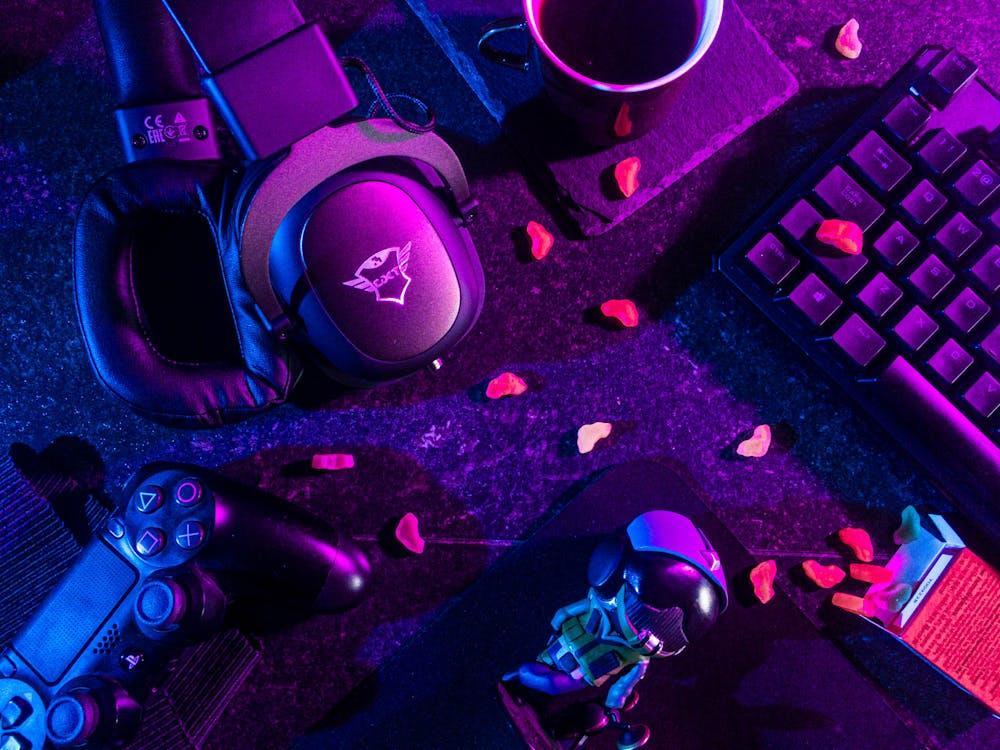 Free Colorful flat lay of gaming gear including headset, controller, and keyboard under vibrant lighting. Stock Photo