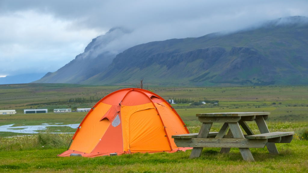 An orange tent pitched by a picnic bench in Iceland during summer.