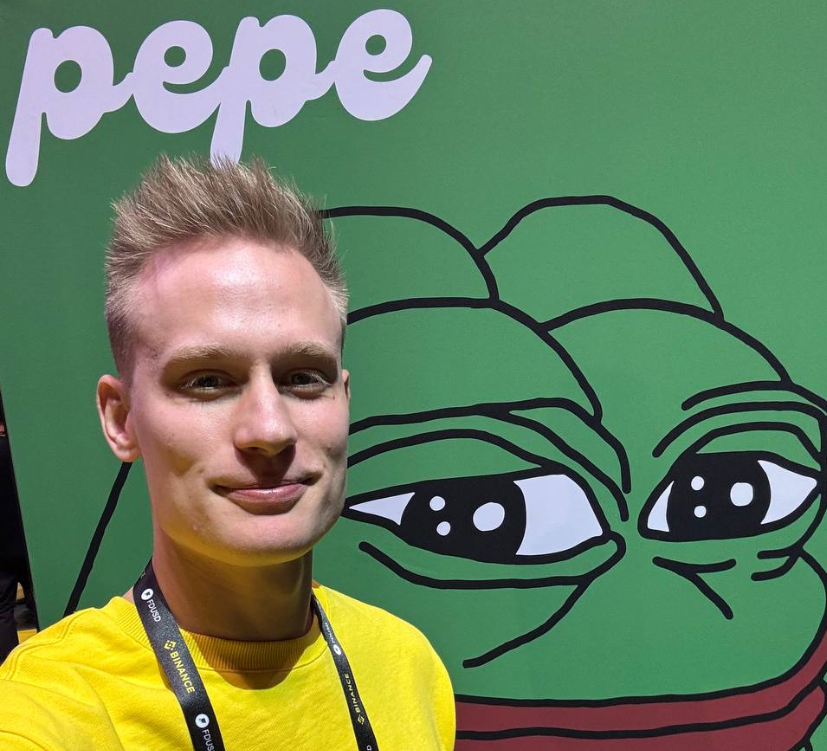 Александр Орловский фото на фоне баннера мемкоина Pepe