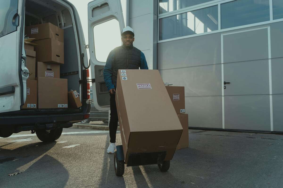 Delivery worker moving a large package with a trolley outside a truck, illustrating efficient last-mile logistics.