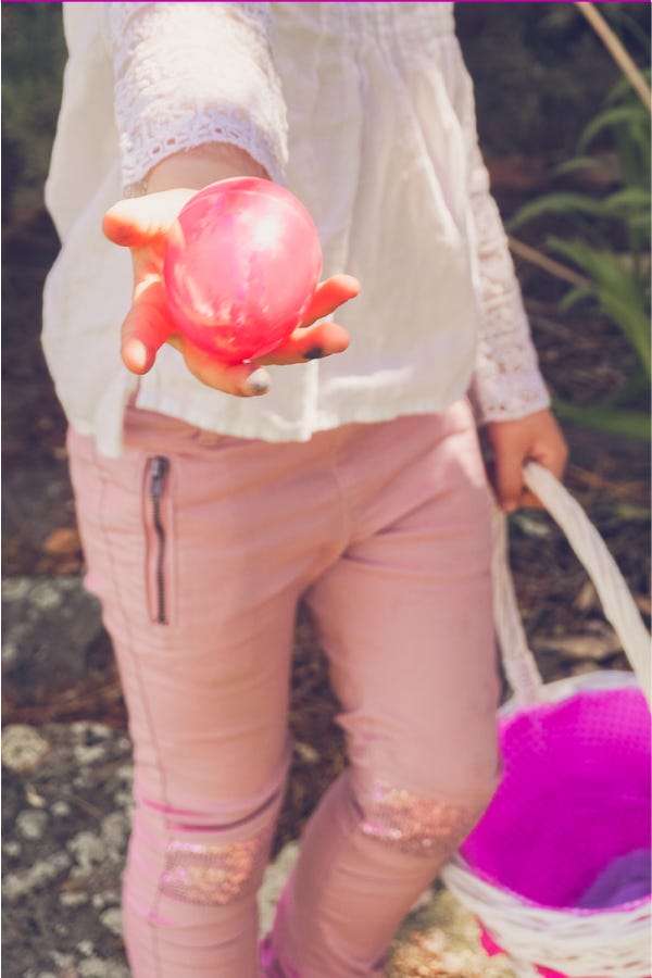 easter egg hunt ideas, young girl holding a pink plastic egg in one hand, and a basket in the other