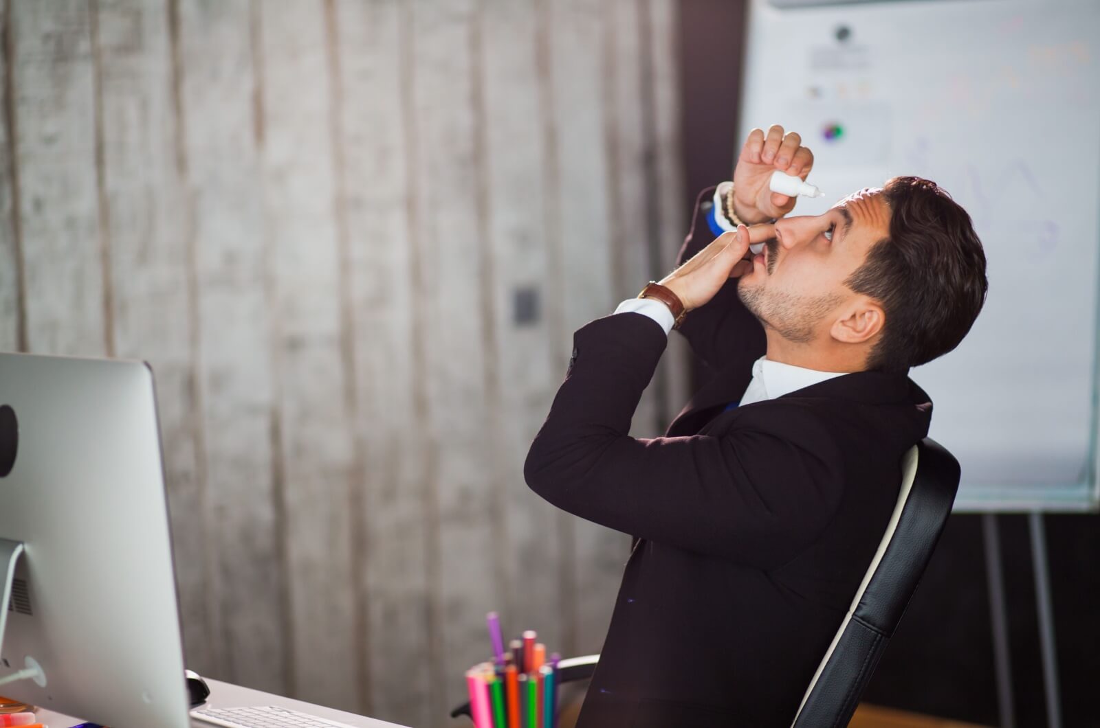 An office worker with dry eyes putting artificial eye drops in their eyes.
