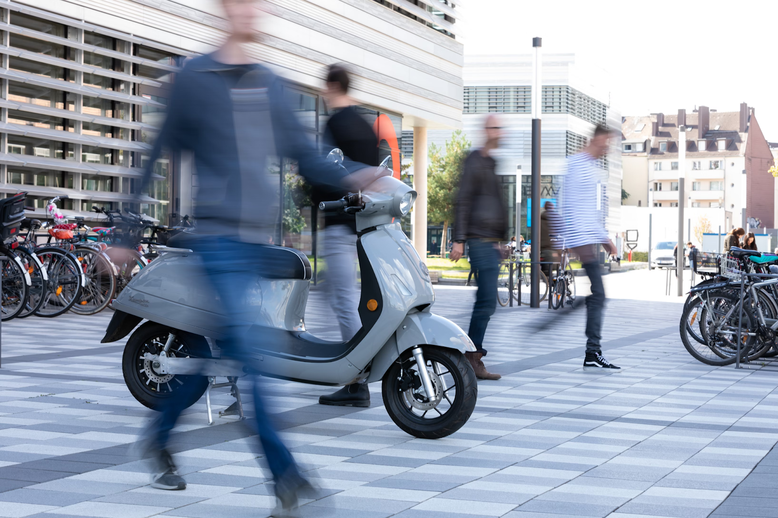 Photo of people blurred in front of a motor bike walking in a city. Image via Pexels