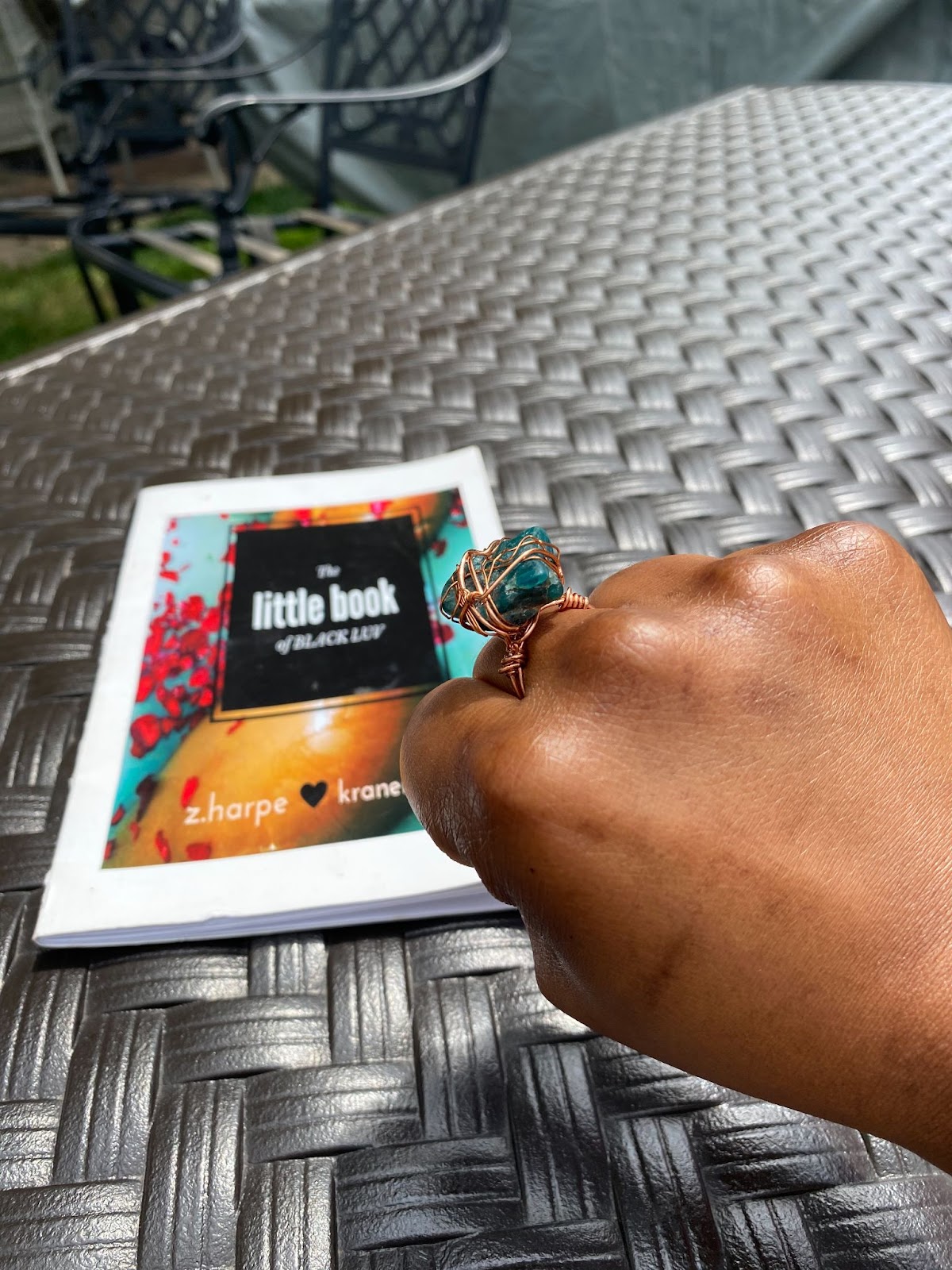 A brown fist with a large ring on the ring finger on top of a book called the little book of black luv.