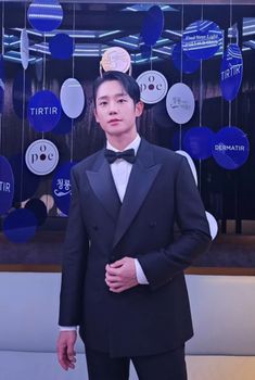 This contains an image of Jung Hae In  in a tuxedo and bow tie standing next to a wall with balloons