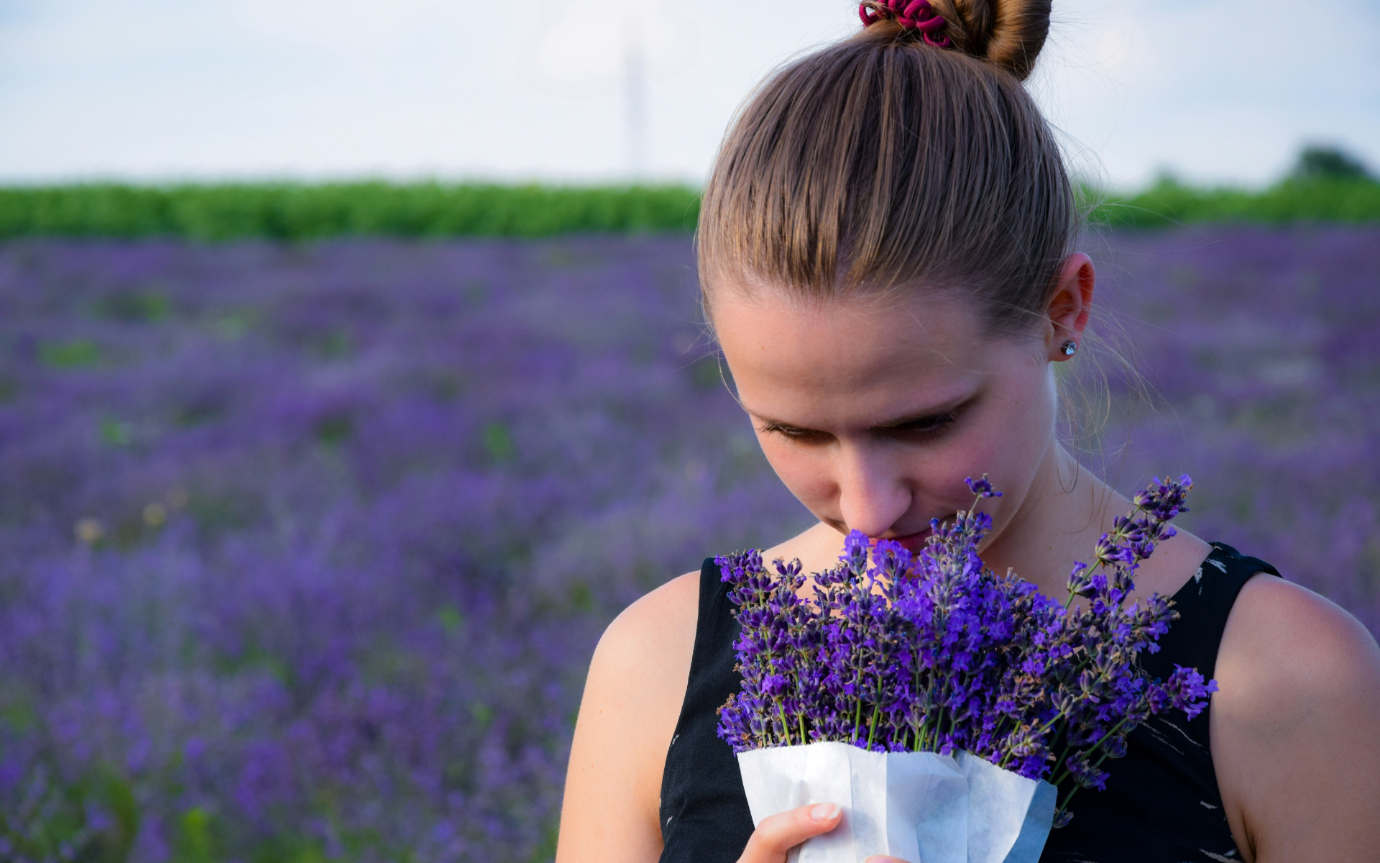 A person smelling a bouquet of purple flowersDescription automatically generated