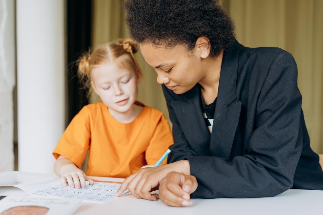 Free A teacher helps a young student with writing tasks at a desk indoors. Stock Photo