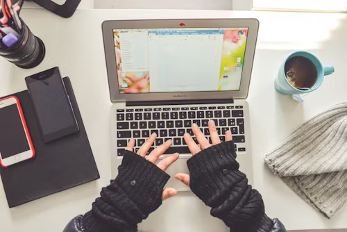 Someone sits typing at an open laptop. There’s a cup of tea on one side a a couple of mobile phones on the other. The user is clearly hard at work researching for their essay