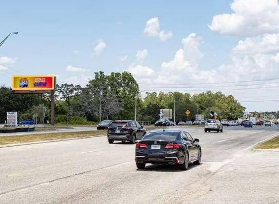 Cars driving on a partly cloudy day with a billboard in the background