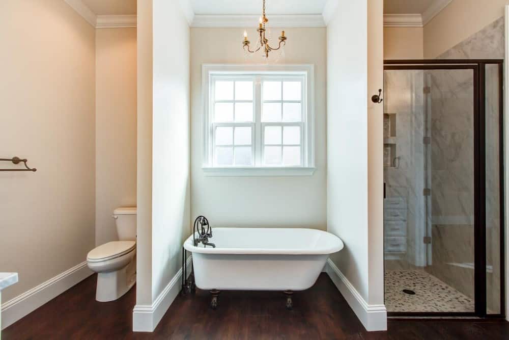 The primary bathroom is equipped with a toilet area, a walk-in shower, and a clawfoot tub topped with a gold chandelier.