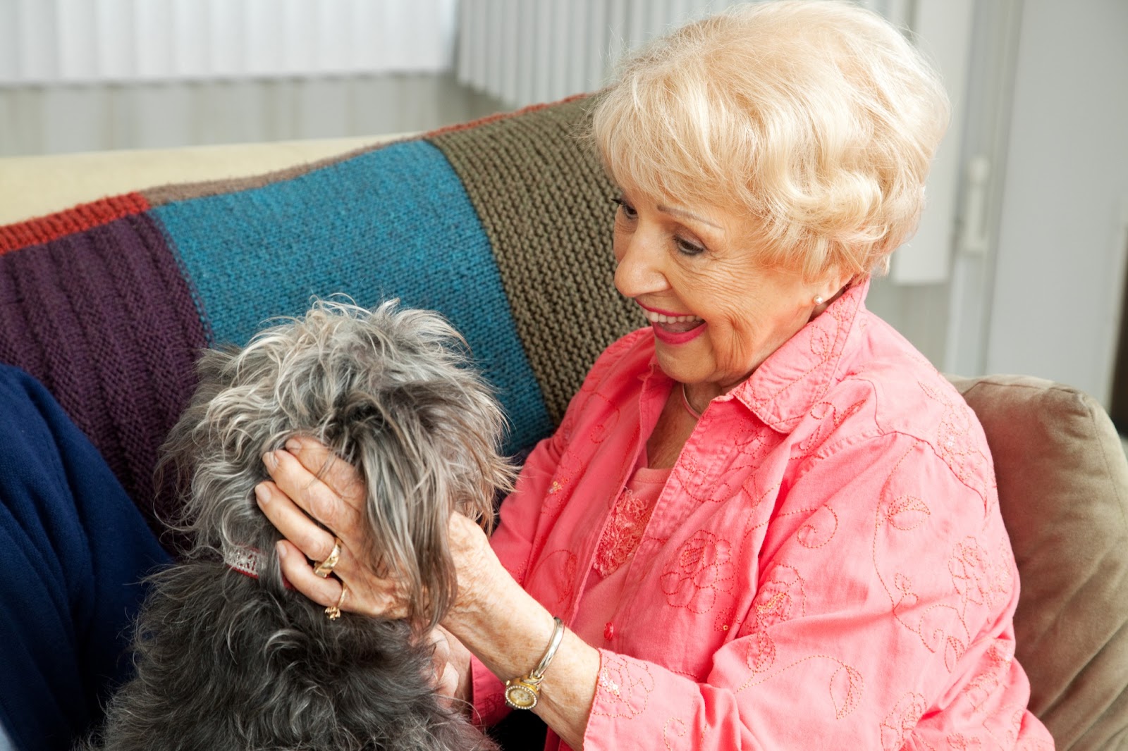 An older adult woman smiling brightly while she pets a little dog.