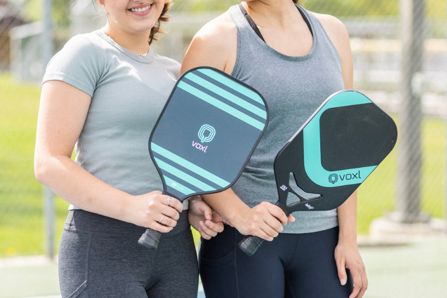 Two pickleball players standing side by side holding Voxl paddles on an outdoor court, smiling and ready to play.