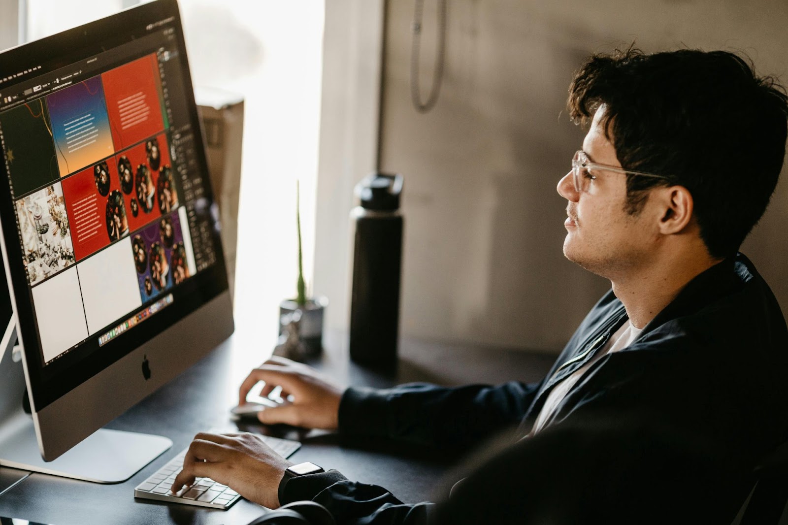 A graphic designer is working on a computer at his desk.