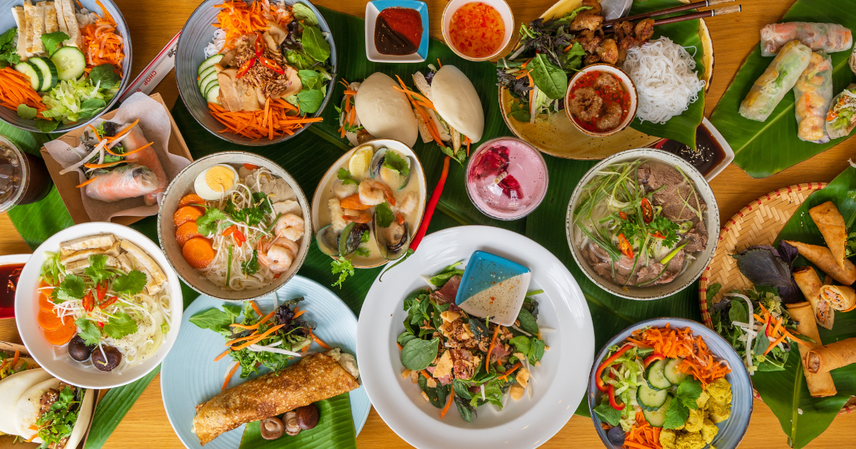 Vibrant Vietnamese feast with pho, spring rolls, vermicelli bowls, banh xeo, and fresh herbs on a beautifully arranged table