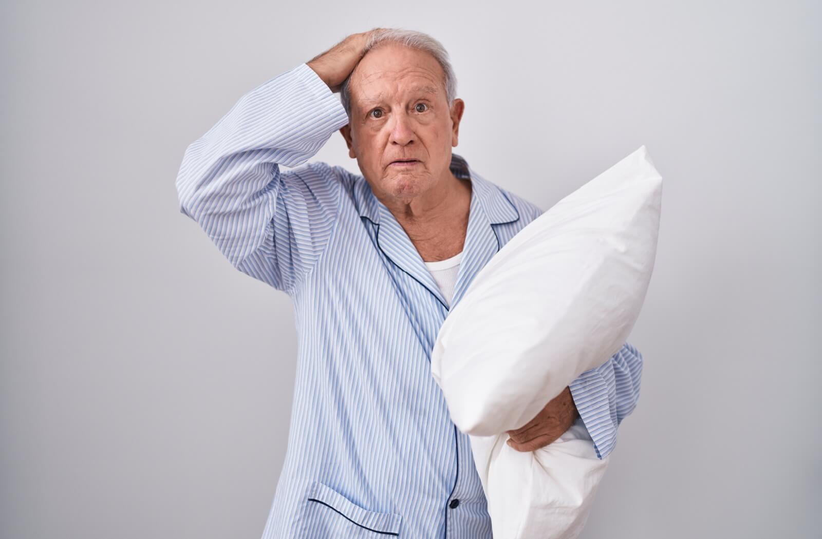 A lost senior in pajamas clutching a pillow holds a hand to their head in confusion.