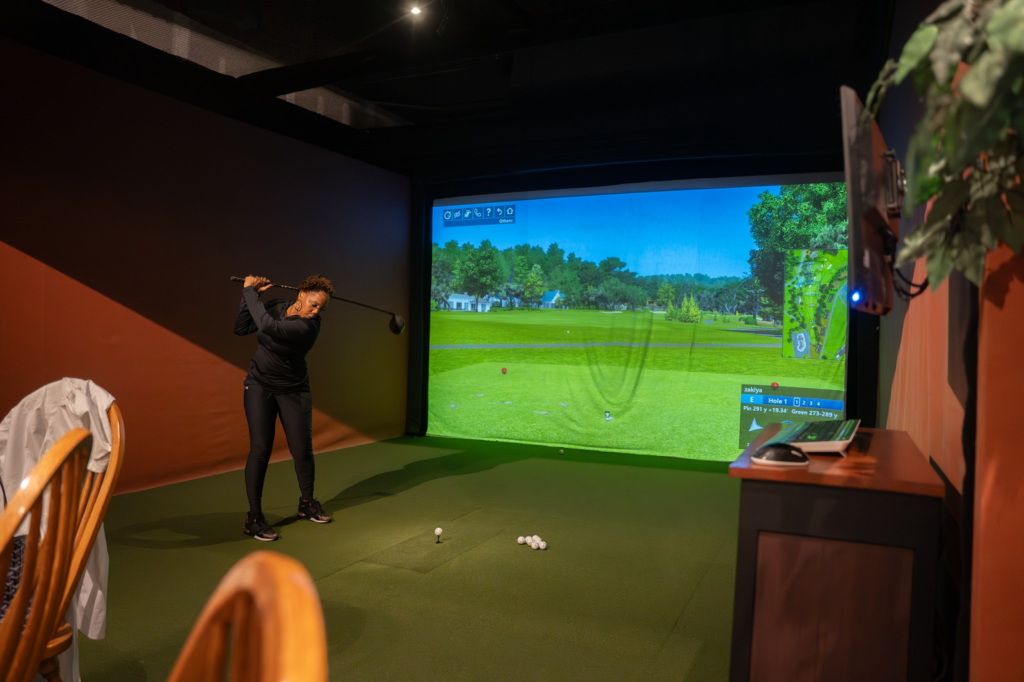 A golfer at a simulator about to swing their golf club