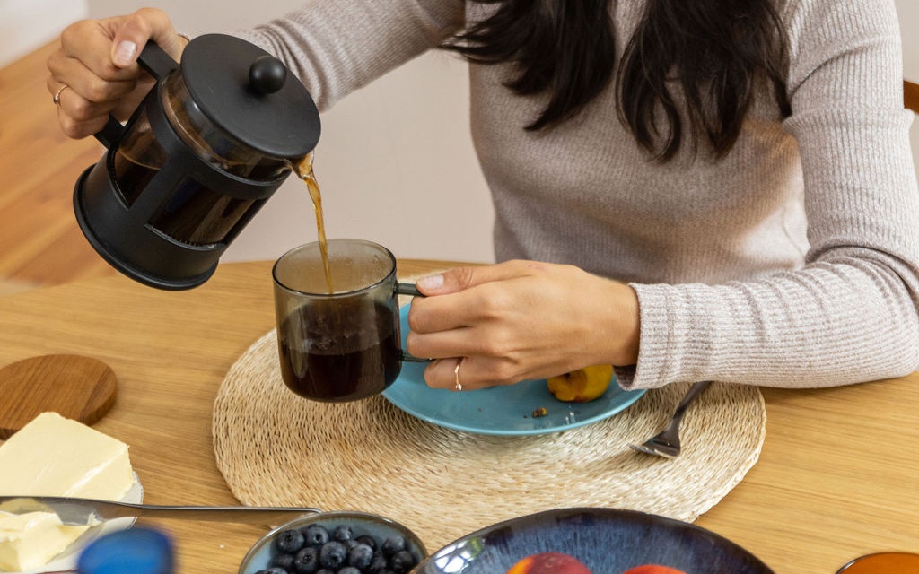 A woman is pouring coffee into a cup at a table, showcasing a moment of calm and enjoyment.