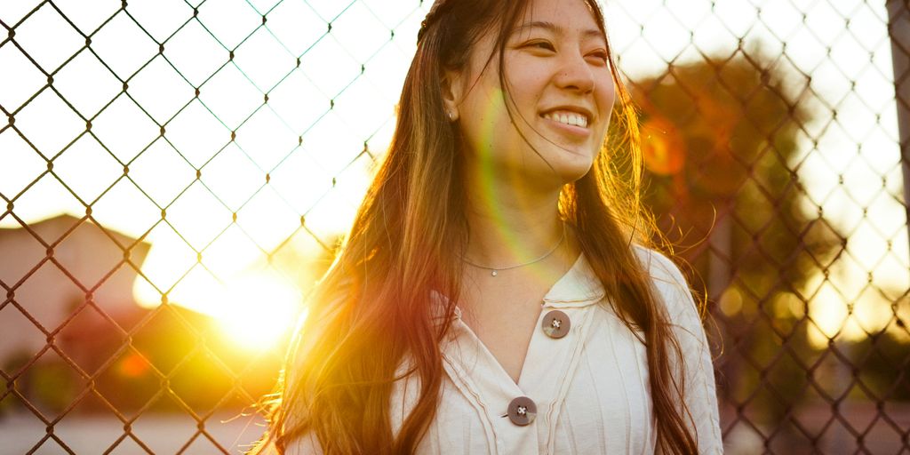 woman smiling in front of chain link fence during golden hour