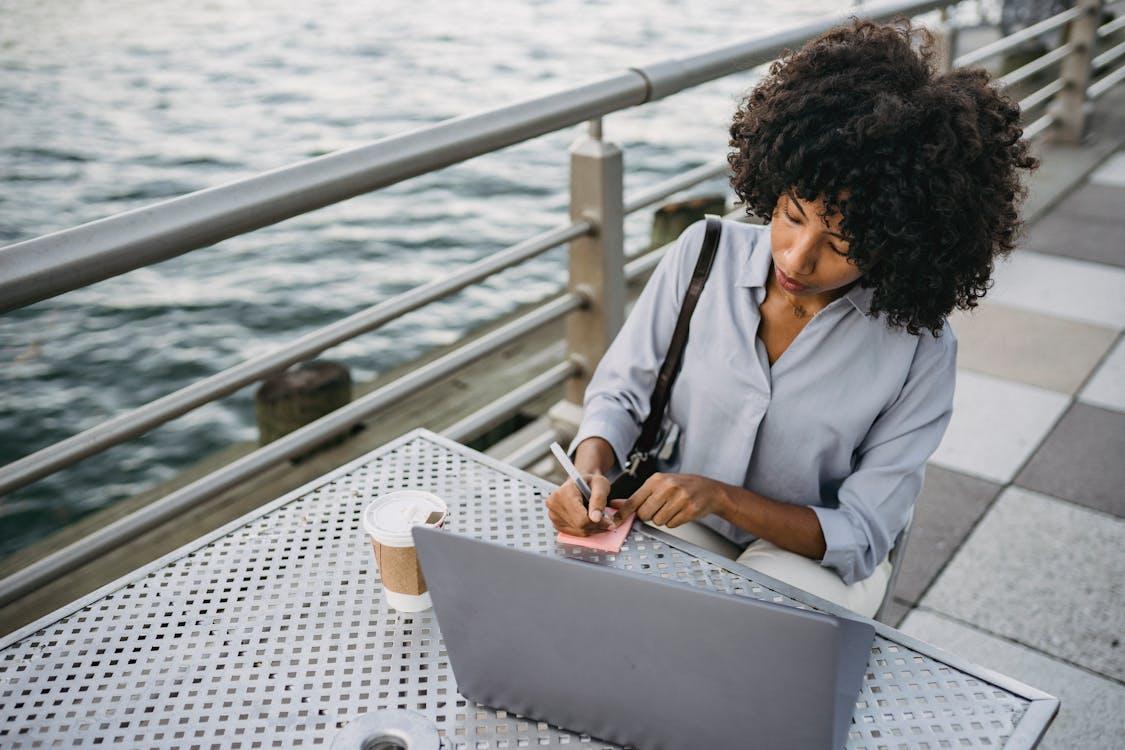 Free Photograph of a Woman with Curly Hair Writing on a Pink Sticky Note Stock Photo