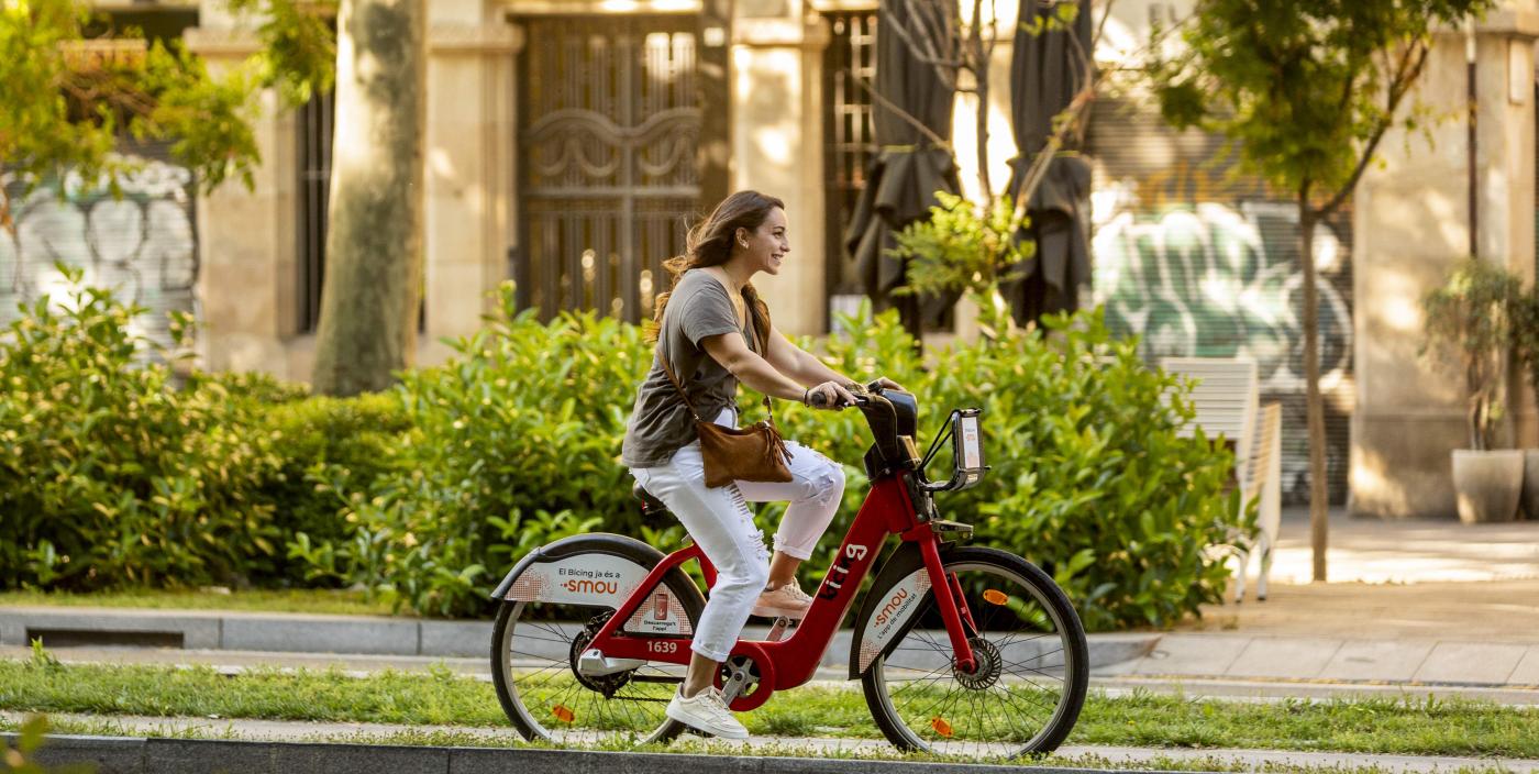 L'utilisateur de Bicing BCN roule avec des pneus Tannus dans une rue verte pleine d'arbres et de plantes, un exemple de mobilité urbaine durable.