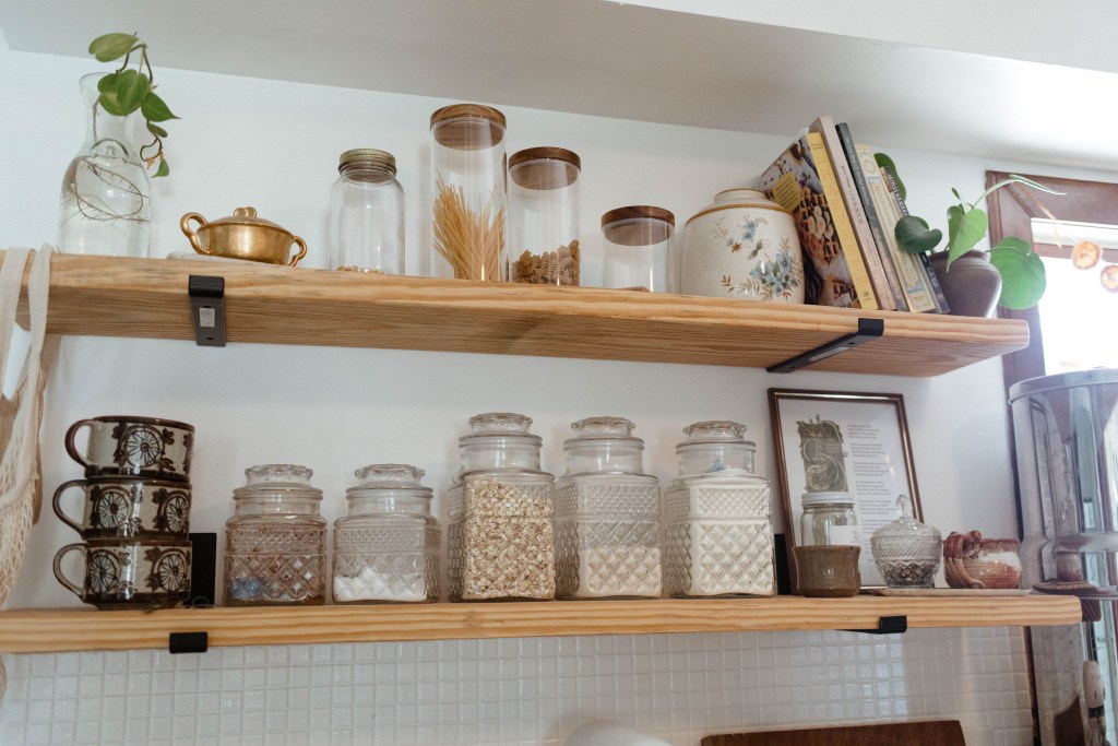 Shelves with glass canisters and mugs and cookbooks. 