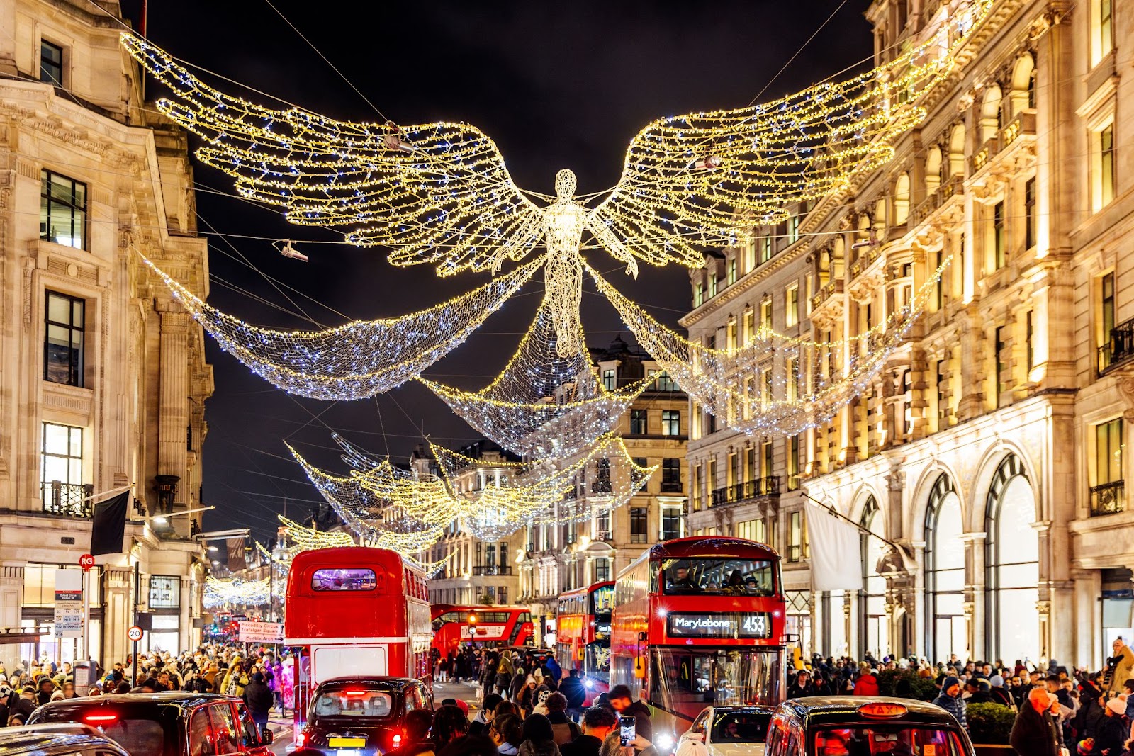 A dazzling Christmas light display on Regent Street, London, with angel-shaped decorations glowing against a dark winter sky