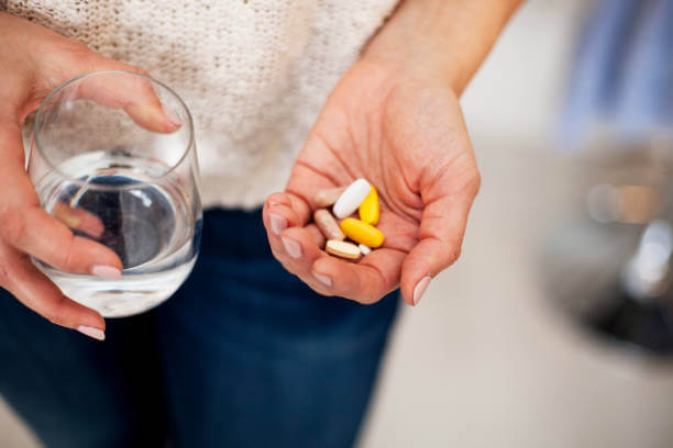 A person holding a glass of water while taking a berberine supplement alongside other vitamins, promoting daily wellness.