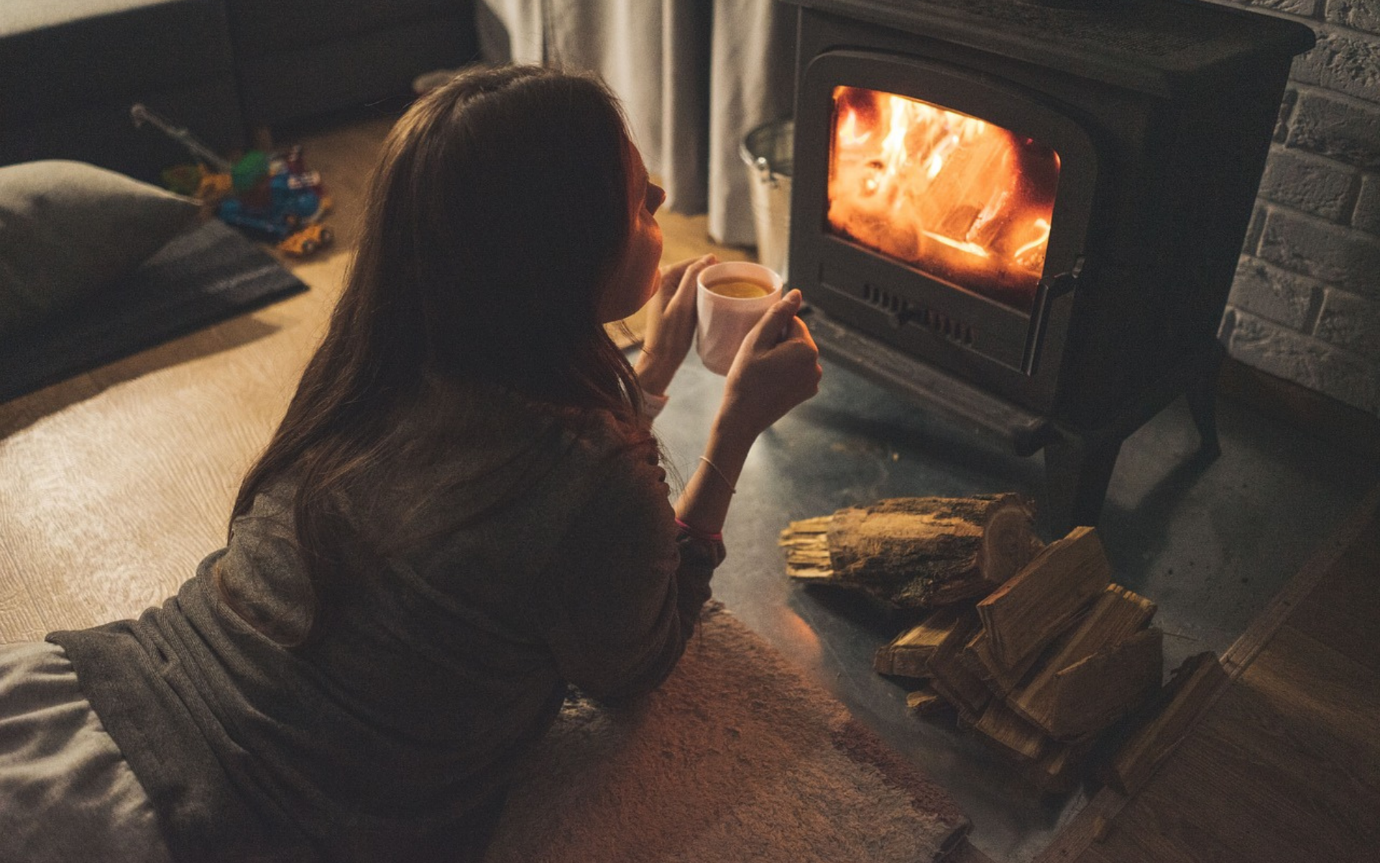 A person sitting on the floor by a fireplace holding a cup of coffeeDescription automatically generated