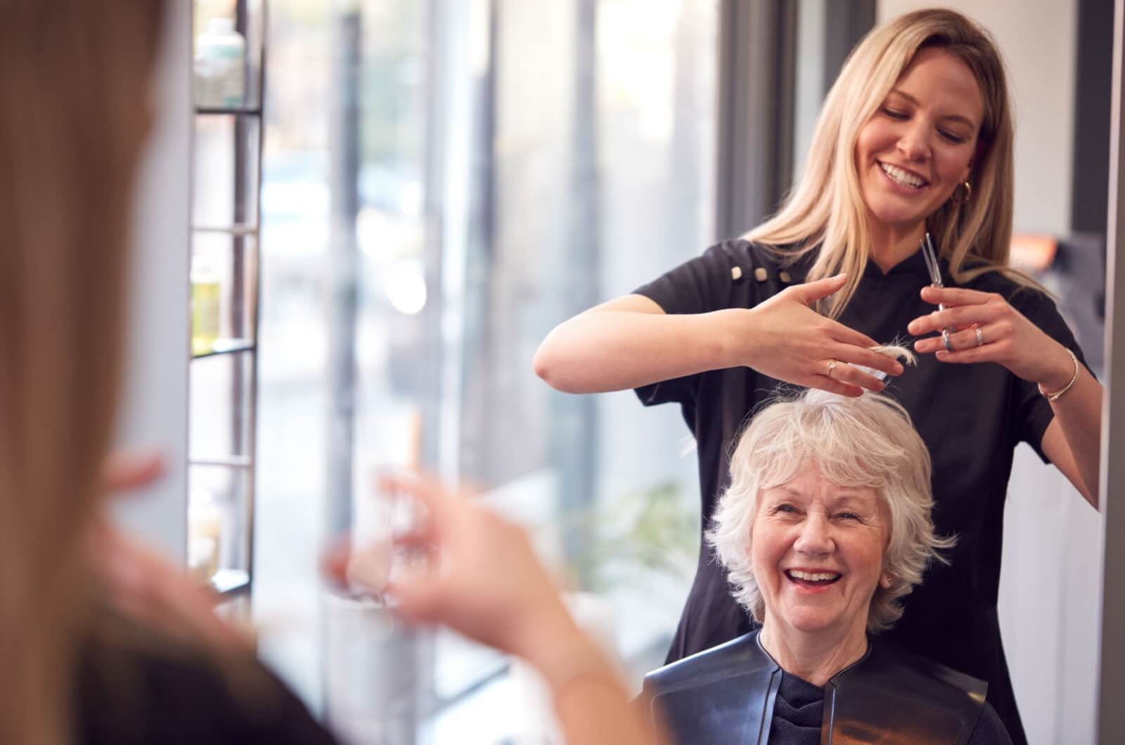 A smiling older woman having her hair cut by a hairstylist.