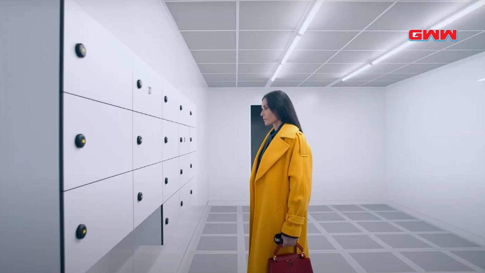 Demi Moore in a yellow coat, standing in front of white lockers