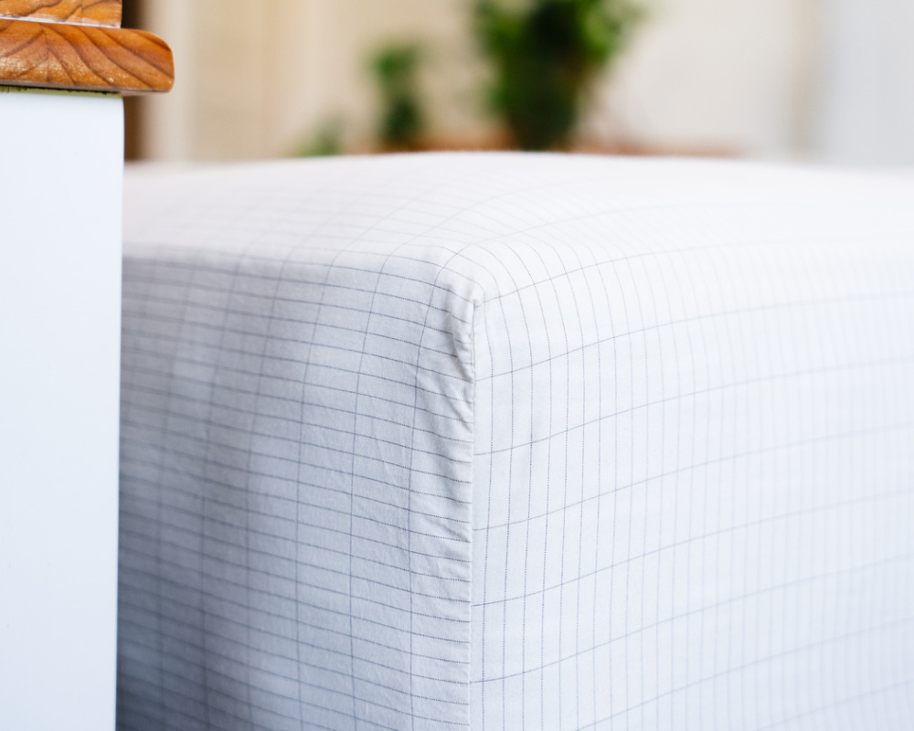 A corner of grounding sheets with a light gray fabric and thin vertical lines, next to a white piece of furniture.