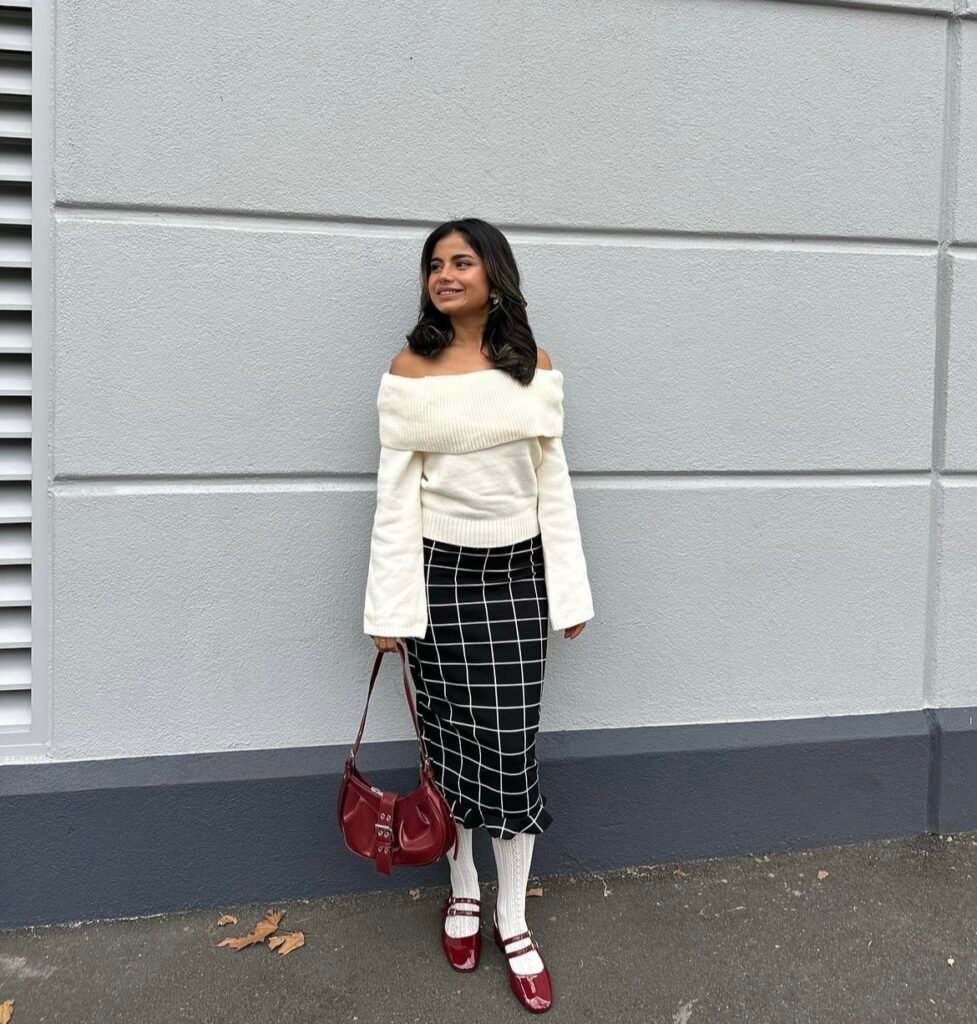 A white sweater with a plaid skirt and a red bag.