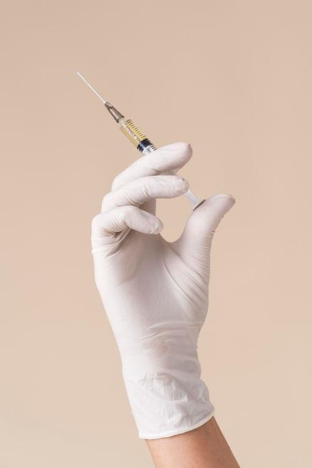 A hand with white glove holding syringe