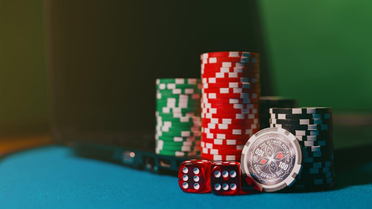 Free Close-up of casino chips and dice on a felt table, next to a laptop for online gambling. Stock Photo