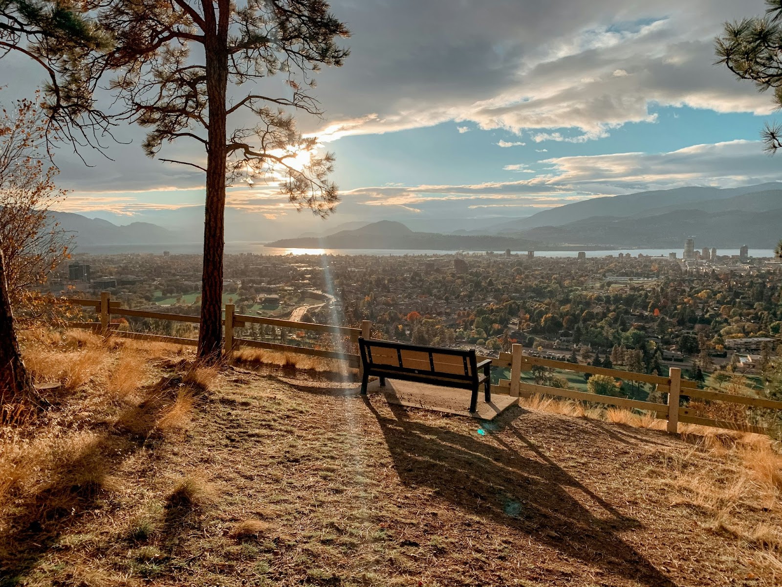 Image of a bench on Knox Mountain overlooking the city of Kelowna and Okanagan Lake with mountains in the background.