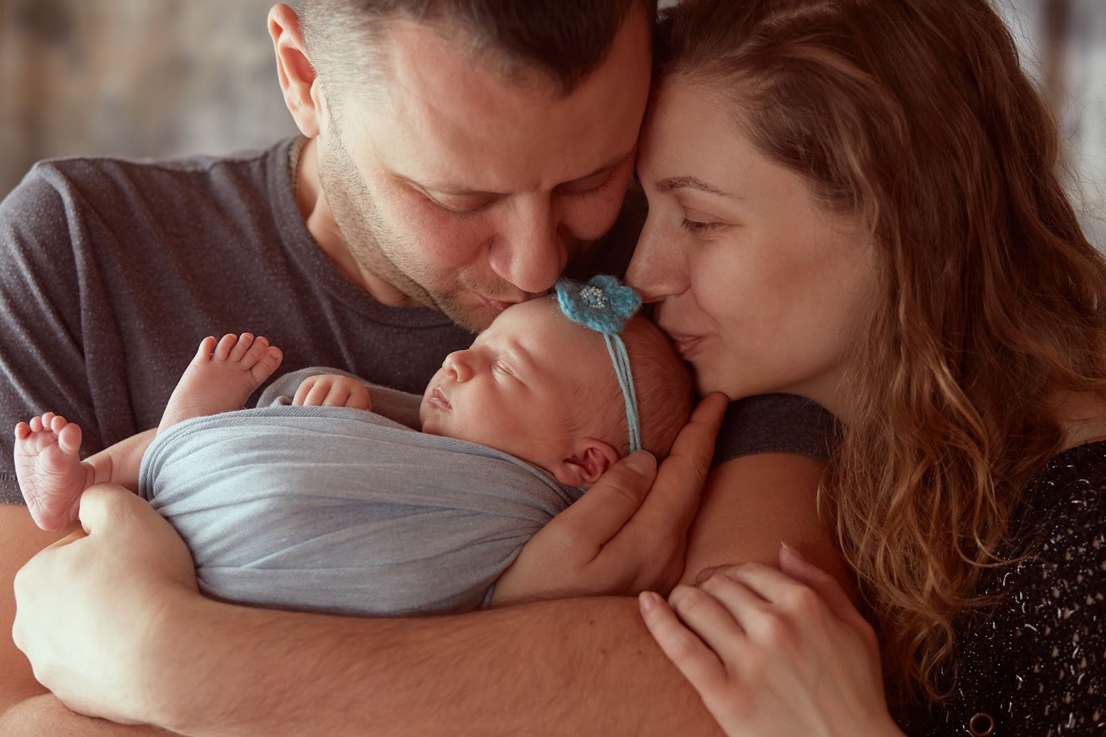 Mom and dad kissing their newborn daughter's forehead