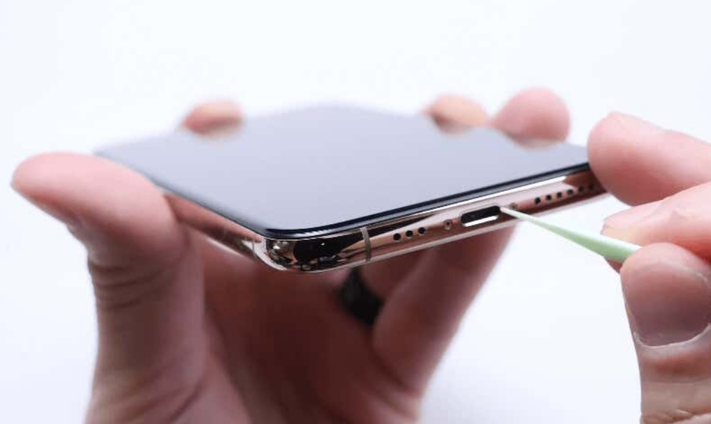 Person cleaning an iPhone port using a small tool