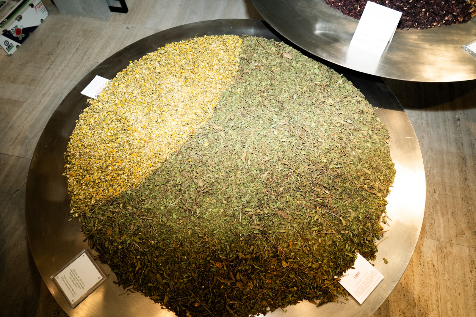 A large, round metal tray showing a blend of chamomile and mint tea leaves in preparation for a tea-blending workshop. 